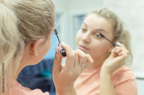 the blonde girl paints her eyelashes with mascara at home in front of the mirror. close up. Selective focus, film grain.