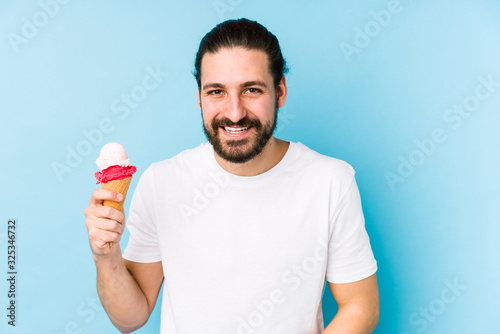 Young caucasian man eating an ice cream isolated laughing and having fun.