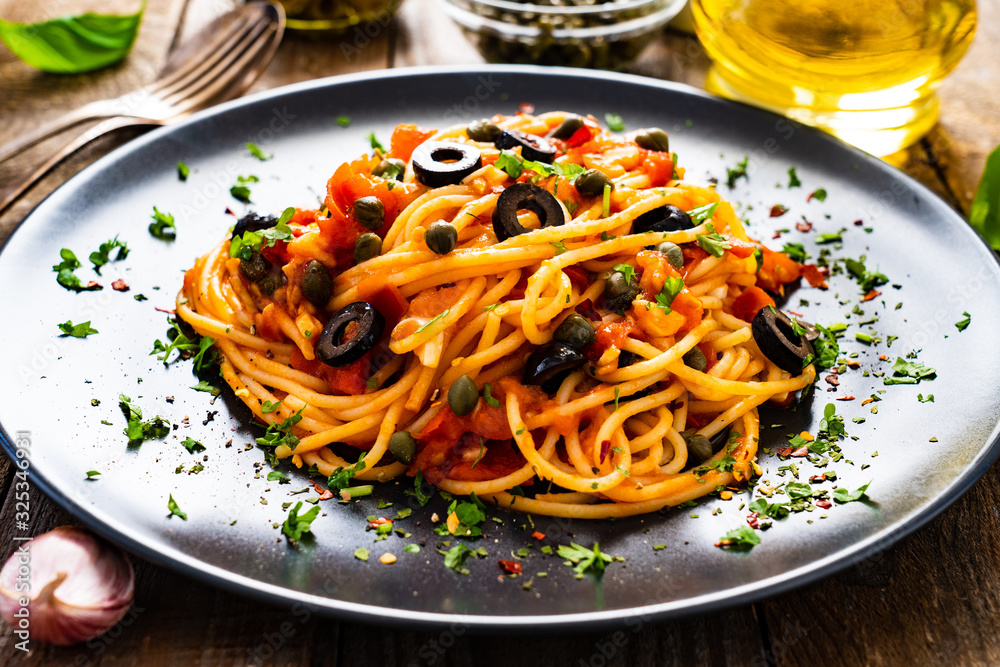 Pasta puttanesca with tomato sauce, anchovies, chilli, capers and olives on wooden table Pasta puttanesca with tomato sauce, anchovies, chilli, capers and olives on wooden table