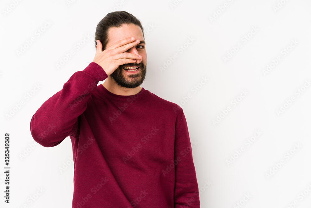 Young long hair man isolated on a white background blink at the camera through fingers, embarrassed covering face. Young long hair man isolated on a white background blink at the camera through fingers, embarrassed covering face.