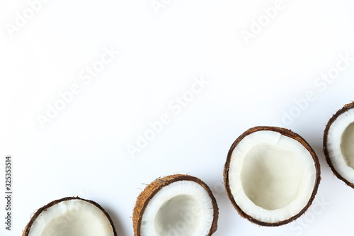 Top view shot of coconuts cracked on halves on paper textured background with a lot of copy space for text. Bacground with raw fruit of tropical palm. Flat lay.