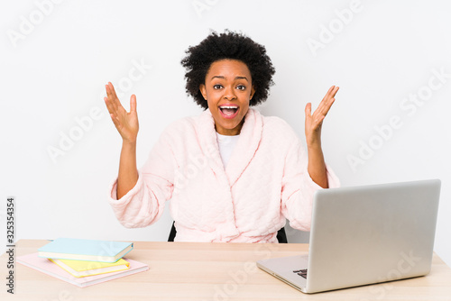 Middle aged african american woman working at home isolated receiving a pleasant surprise, excited and raising hands.