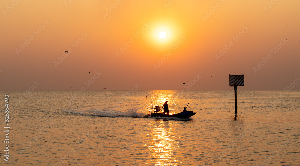 sun going down at the shore with silhouette boat