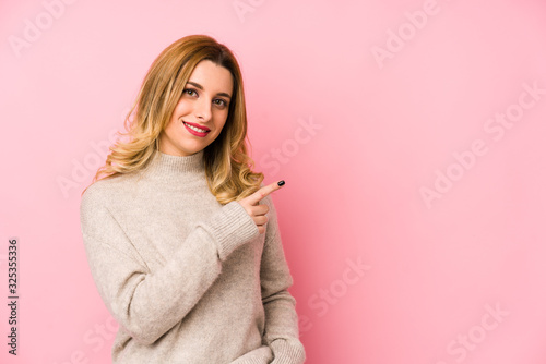 Young blonde cute woman wearing a sweater isolated smiling and pointing aside, showing something at blank space.
