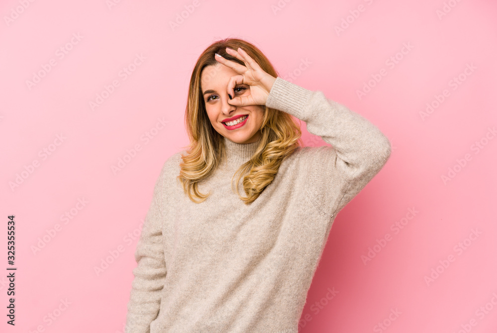Young blonde cute woman wearing a sweater isolated excited keeping ok gesture on eye. Young blonde cute woman wearing a sweater isolated excited keeping ok gesture on eye.