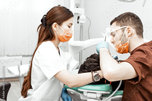 A young male dentist doctor treats a patient. Medical manipulations in dentistry  surgery. Professional uniform and equipment of a dentist. Healthcare Equipping a doctor   s workplace. Dentistry