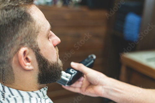 Beauty shop for men. Shaving a beard in a barbershop. Barber cuts his beard with a razor and clipper. close up Brutal haircuts. Hairdresser equipment. Selective focus.