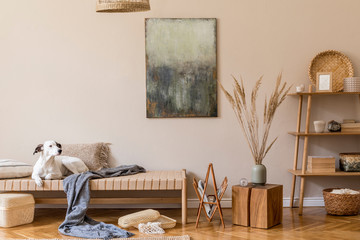 Boho composition of living room with furnitures, mock up paintings, rattan decoration, bamboo shelf with elegant personal accessories. Beautiful dog lying on the chaise longue. Home decor Template