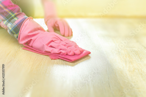 A female hand in a pink glove holds a soft rag, wipes the wooden floor from dust and dirt. House cleaning, washing surfaces from light laminate, the concept of cleanliness. Background, copy space.