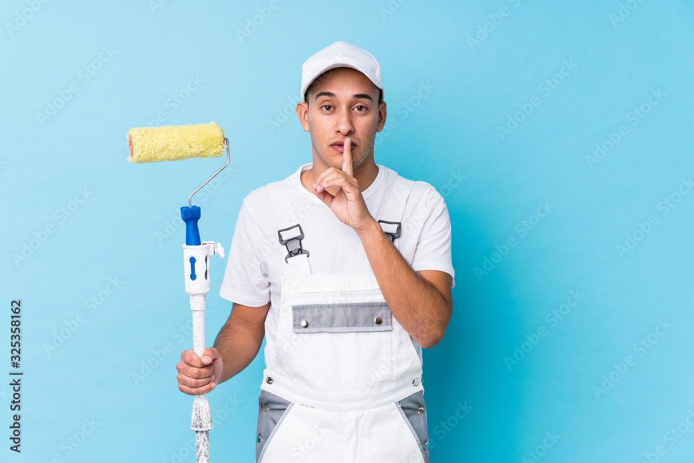 Young professional painter latin man isolated keeping a secret or asking for silence. Young professional painter latin man isolated keeping a secret or asking for silence.
