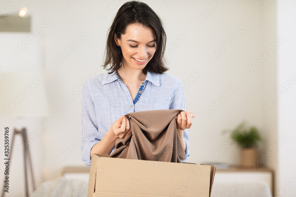 Happy young girl packing clothes in cardboard box Happy young girl packing clothes in cardboard box