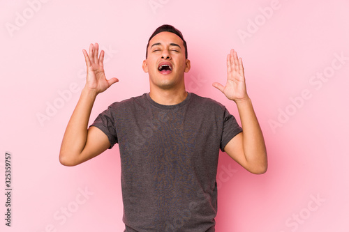 Yooung latin man posing in a pink backgroundscreaming to the sky, looking up, frustrated. photo