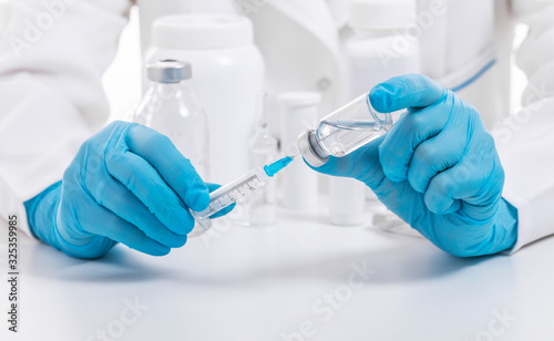 Unrecognizable doctor wearing medical protective mask and blue nitrile gloves fills syringe, cropped