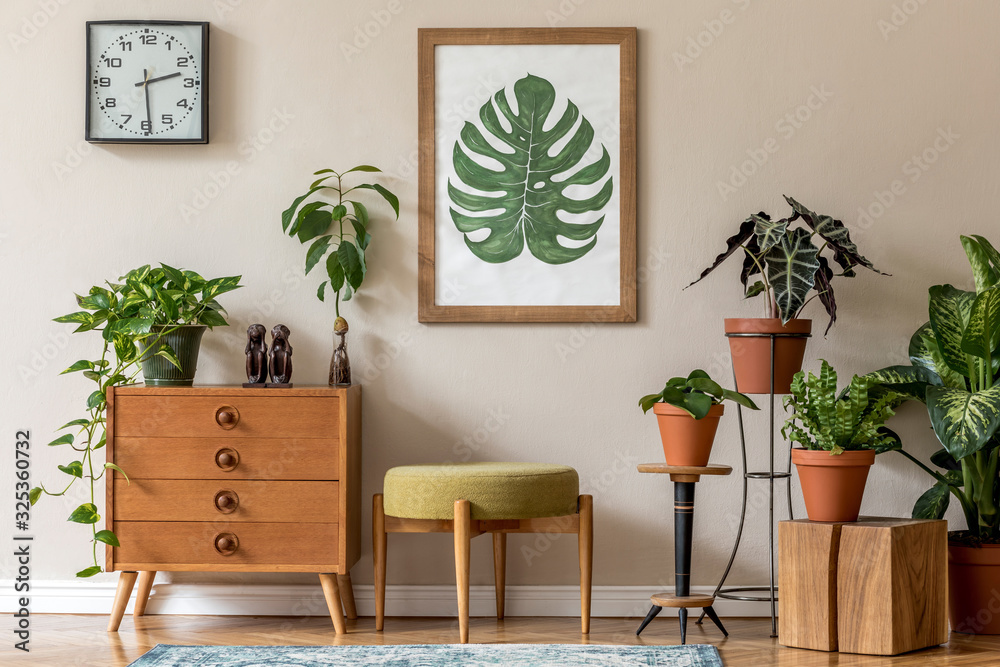 Vintage interior design of living room with stylish retro furnitures, a lot of plants, commode, black clock and brown poster mock up frame on the beige wall. Stylish home decor. Template.  - obrazy, fototapety, plakaty 