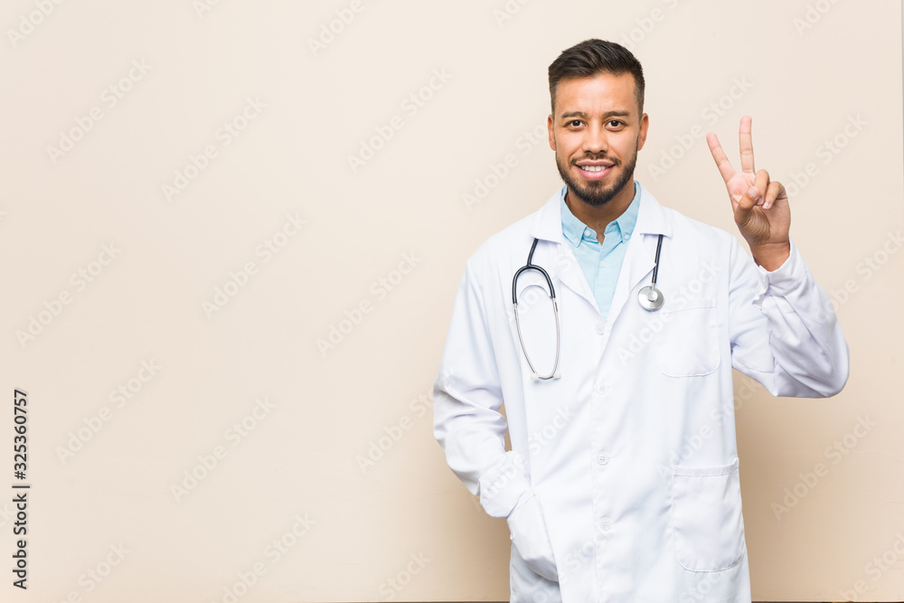Young south-asian doctor man showing number two with fingers. Young south-asian doctor man showing number two with fingers.
