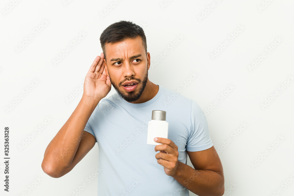 Young south-asian man holding an after shave cream trying to listening a gossip. Young south-asian man holding an after shave cream trying to listening a gossip.