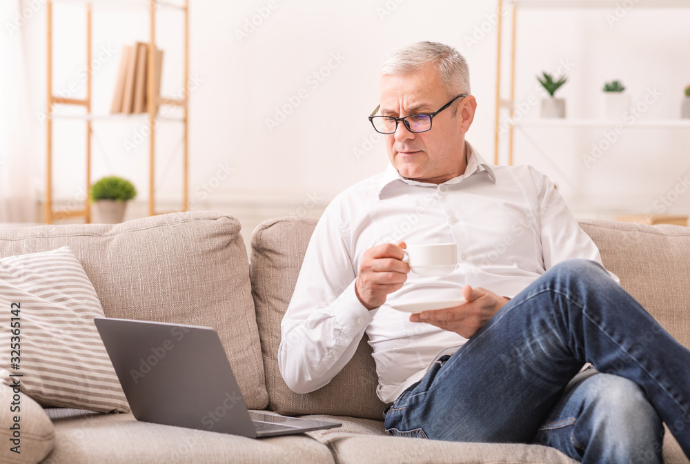 Elderly Man Looking At Laptop And Having Tea