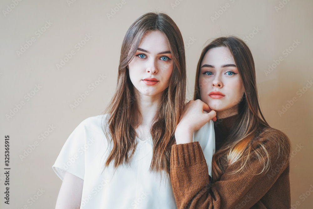 Young beautiful long hair girls sisters twins in casual isolated on beige background Young beautiful long hair girls sisters twins in casual isolated on beige background