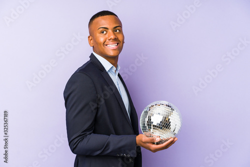 Young latin man holding a ball party isolated looks aside smiling, cheerful and pleasant.