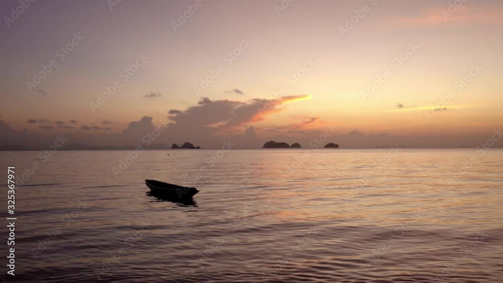 A wooden boat sways on the waves of the ocean near the shore. Big rock in the water on background. Tropical island Romance by the ocean. Tropical landscape A wooden boat sways on the waves of the ocean near the shore. Big rock in the water on background. Tropical island Romance by the ocean. Tropical landscape