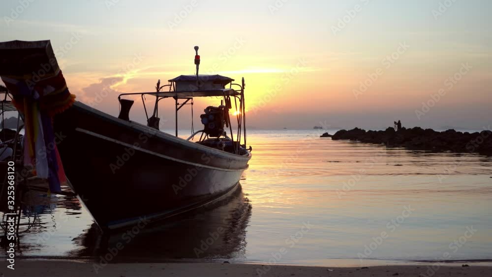 Boat sways in bay at coast of a tropical island. Evening, sunset in the ocean. Tropical landscape. Light waves rock the boat. People on sup board swim to shore Boat sways in bay at coast of a tropical island. Evening, sunset in the ocean. Tropical landscape. Light waves rock the boat. People on sup board swim to shore