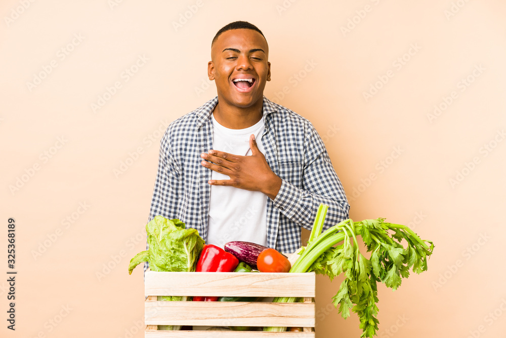 Young farmer man isolated on a beige background laughs out loudly keeping hand on chest. Young farmer man isolated on a beige background laughs out loudly keeping hand on chest.