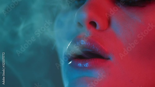 drunk or stoned sexy girl with pleasure breathe cigarette or hemp smoke, dramatic scene in slow motion woman is high smoking joint or tobacco at party or near neon sign