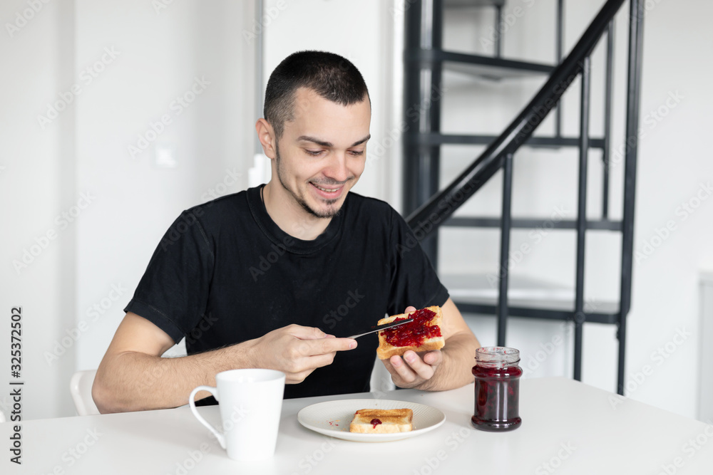 The guy has breakfast with toast with jam. The guy has breakfast with toast with jam.