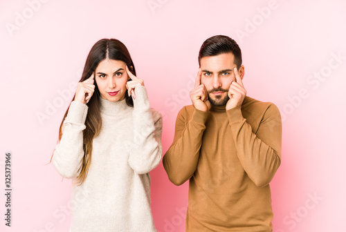 Young caucasian couple isolated focused on a task, keeping forefingers pointing head.