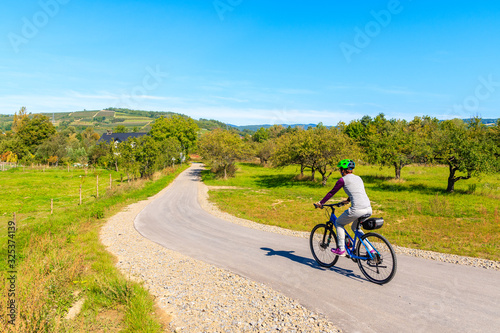 Young woman cycling on Velo Dunajec road among green hills with orchards near Nowy Sacz town, Beskid Sadecki Mountains, Poland