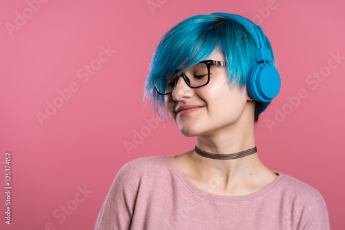 Pretty young girl with turquoise hair having fun, smiling, dancing with blue headphones in studio on colorful background. Music, dance, radio concept.