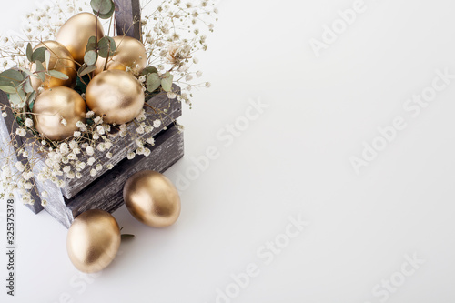 Golden eggs with spring flowers on a white background, with copy space. The concept of Easter and the symbol of the holiday.