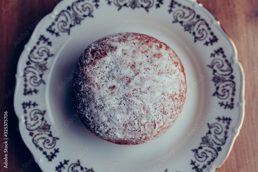 Fresh homemade jelly filled doughnut on a plate, covered in powdered sugar, above view Fresh homemade jelly filled doughnut on a plate, covered in powdered sugar, above view