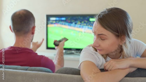 An offended woman sits next to a guy watching a game on TV photo