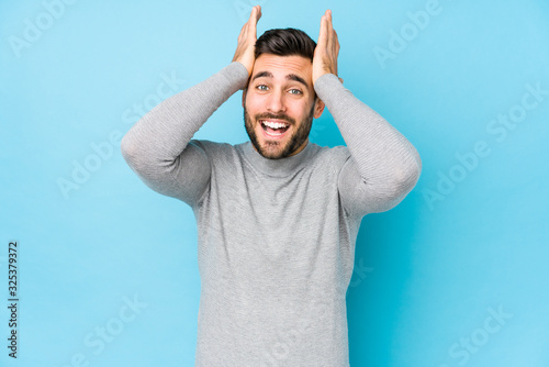 Young caucasian man against a blue background isolated laughs joyfully keeping hands on head. Happiness concept.