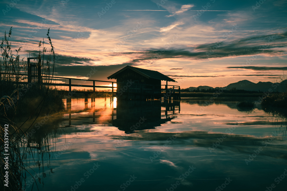 lonely boathouse on a lake with a pier while sun is rising