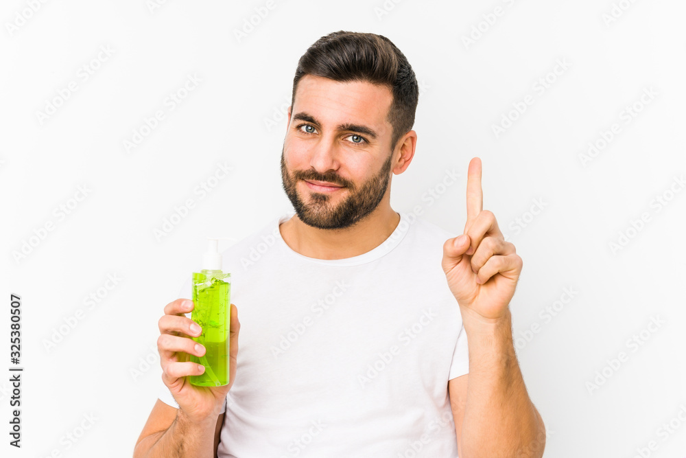 Young caucasian man holding a moisturizer with aloe vera isolated showing number one with finger. Young caucasian man holding a moisturizer with aloe vera isolated showing number one with finger.