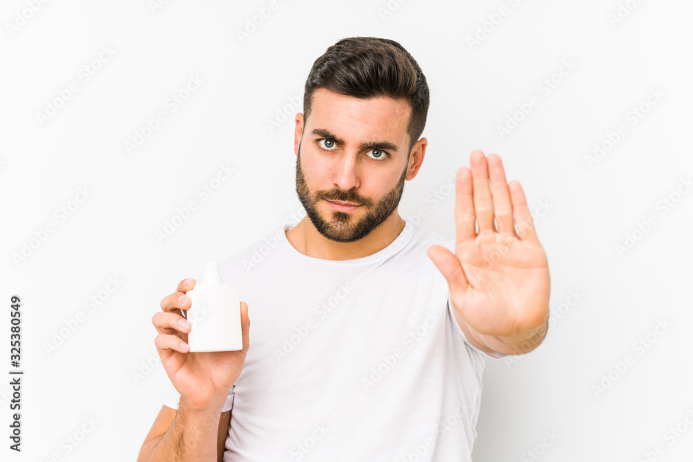 Young caucasian man holding a vitamins bottle isolated standing with outstretched hand showing stop sign, preventing you. Young caucasian man holding a vitamins bottle isolated standing with outstretched hand showing stop sign, preventing you.