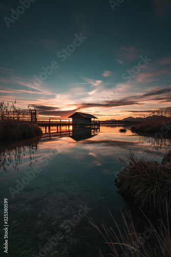 lonely boathouse on a lake with a pier while sun is rising