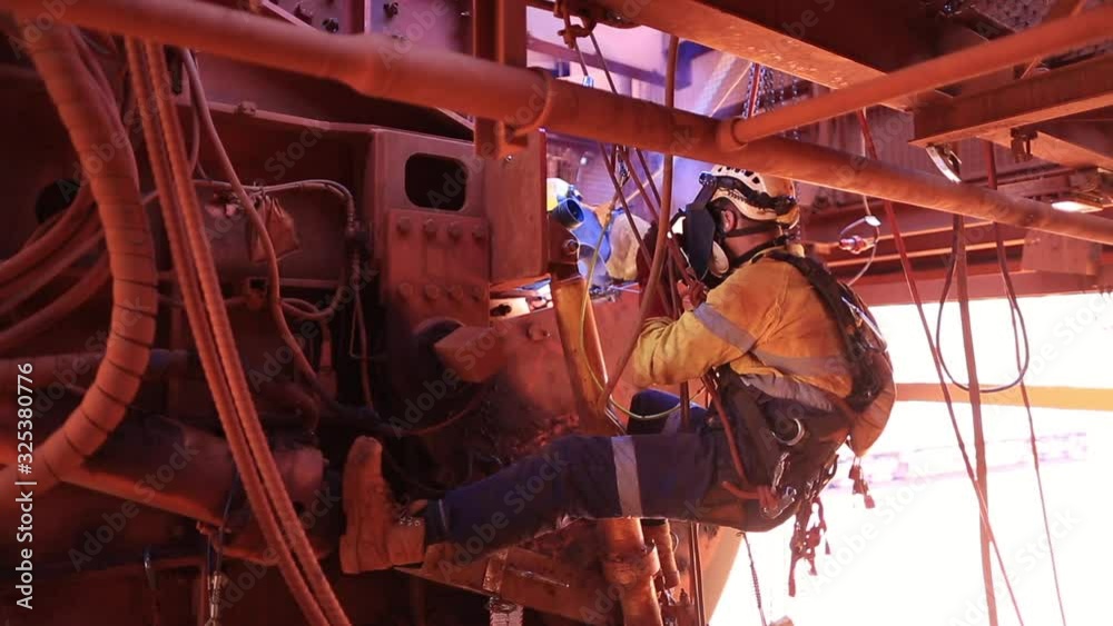 Footage of male rope access welder wearing safety equipment, glove protection working on twin rope abseiling performing welding maintenance structures metal repairs on construction site, Perth, OZ