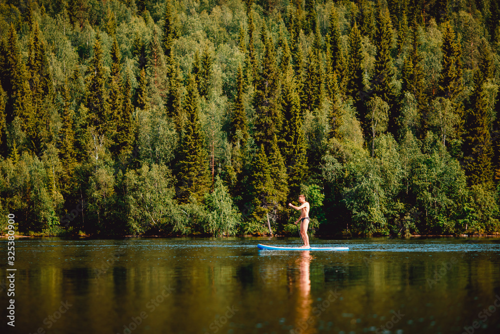 Fototapeta premium Man rowing oar on sup board blue lake water paddleboard background of forest