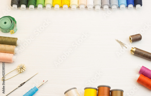 Copyspace frame with sewing tools, multi-colored threads and accessories on a white wooden background, top view