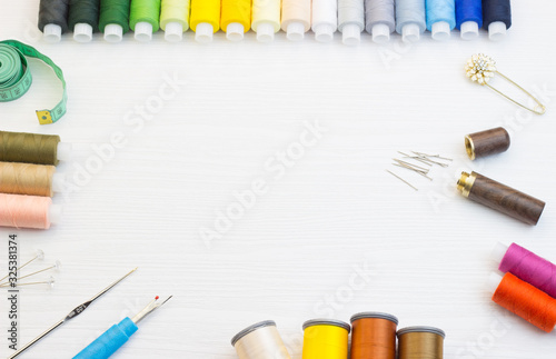 Copyspace frame with sewing tools, multi-colored threads and accessories on a white wooden background, top view