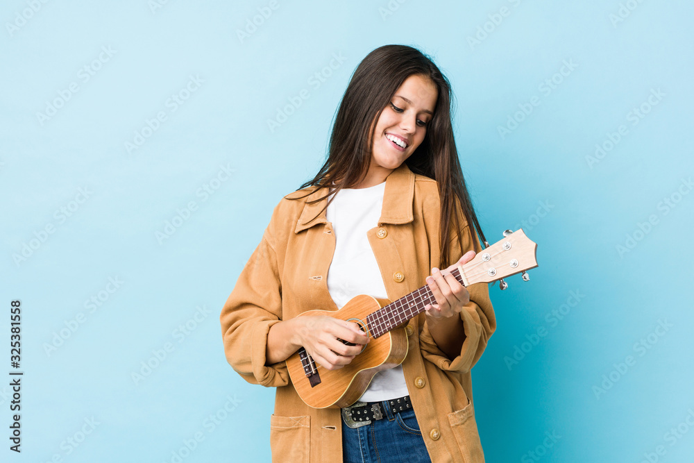 Young caucasian woman playing ukelele isolated on a blue background Young caucasian woman playing ukelele isolated on a blue background