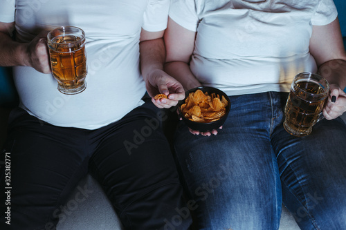 Emotional eating, alcohol addiction, depression, relationship problems. Overweight couple watching tv eating junk food and beer late in the night. Nerve food