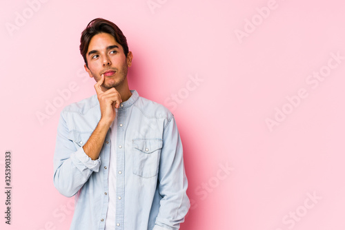 Young caucasian man posing in a pink background isolated looking sideways with doubtful and skeptical expression.