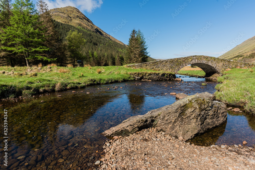 Fototapeta premium Ancient stone bridge crossing a tranquil river in Scotland
