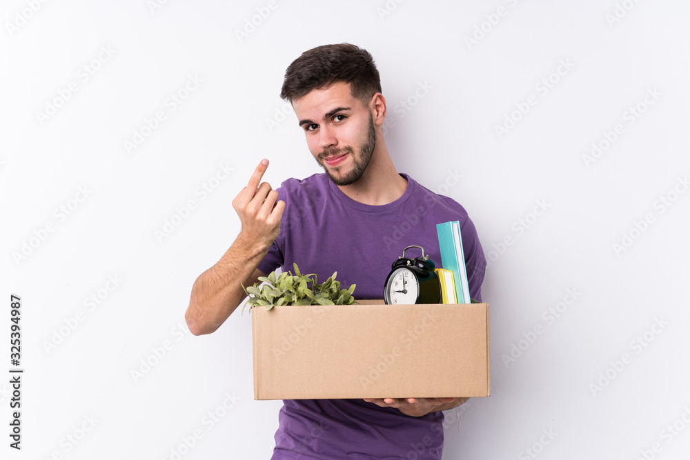 Young caucasian man moving a new home isolated pointing with finger at you as if inviting come closer. Young caucasian man moving a new home isolated pointing with finger at you as if inviting come closer.