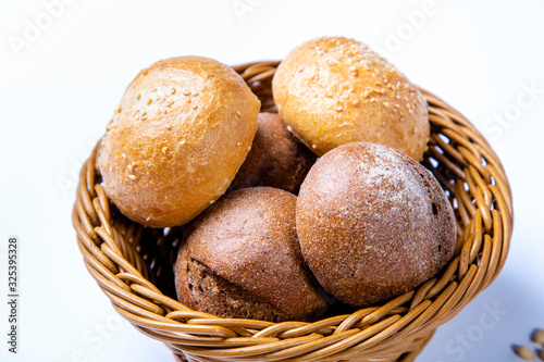 Wicker bread basket with white and rye round loaves. On white background.