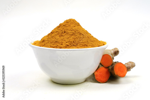 Turmeric powder in a white cup and turmeric root isolated on a white background, used as a tonic for the body and turmeric supplements or as an ingredient in food. Turmeric has anti-oxidants which hel